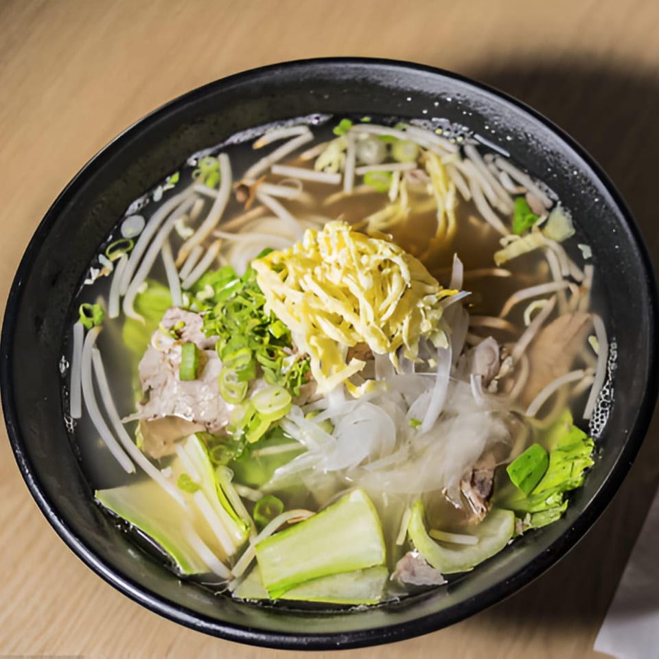 A black bowl of Garionban's Korean noodle soup with shredded egg, green onions, and vegetables.