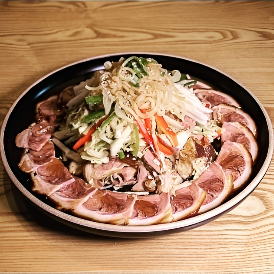A black plate of Garionban's Korean Jokbal, sliced pork hock, topped with fresh vegetables and sesame seeds.